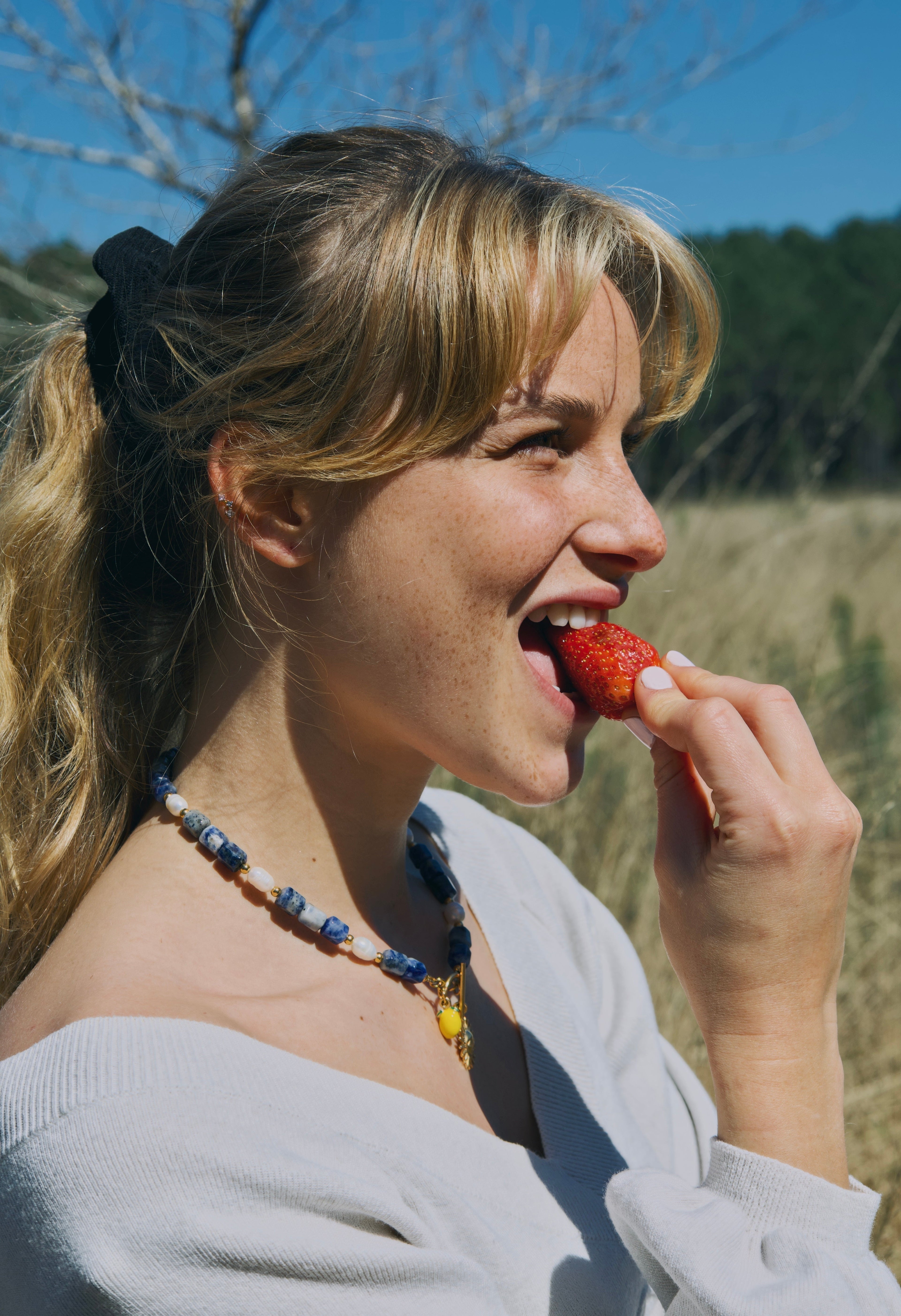 jeune femme blonde qui porte un collier fait main en pierres naturelles entrain de manger une fraise